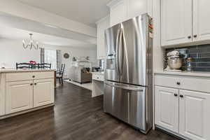 Kitchen with a notable chandelier, stainless steel fridge, pendant lighting, decorative backsplash, and white cabinets