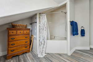 Bathroom featuring vaulted ceiling, wood-type flooring, and shower / tub combo with curtain