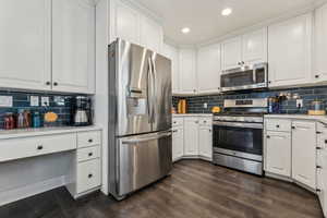 Kitchen featuring stainless steel appliances, white cabinetry, tasteful backsplash, and dark wood-type flooring