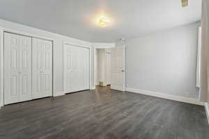 Unfurnished bedroom featuring dark hardwood / wood-style flooring and two closets