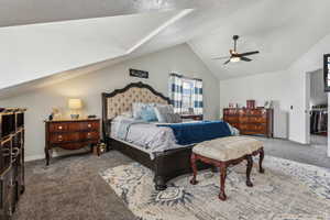 Carpeted bedroom featuring ceiling fan, a textured ceiling, and vaulted ceiling