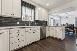 Kitchen with kitchen peninsula, decorative backsplash, stainless steel dishwasher, sink, and white cabinetry