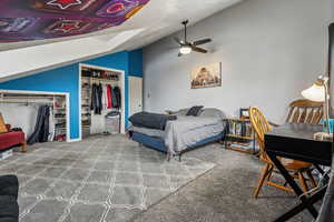 Bedroom with carpet, two closets, vaulted ceiling, ceiling fan, and a textured ceiling