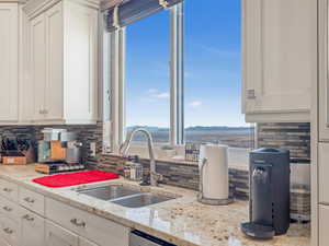 Kitchen featuring light stone counters, white cabinetry, and sink