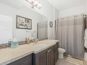 Full bathroom with decorative backsplash, vanity, toilet, and shower / bathtub combination with curtain