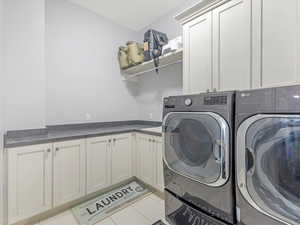 Laundry room with washing machine and clothes dryer, light tile patterned floors, and cabinets