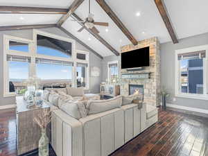 Living room featuring plenty of natural light, lofted ceiling with beams, a stone fireplace, and ceiling fan