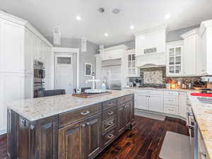 Kitchen featuring dark brown cabinetry, hanging light fixtures, stainless steel appliances, decorative backsplash, and a kitchen island