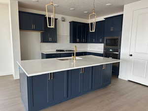 Kitchen featuring wall oven, light wood-type flooring, a center island with sink, and built in microwave