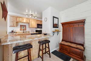 Kitchen featuring black appliances, a kitchen bar, kitchen peninsula, and light brown cabinets