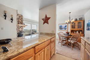 Kitchen featuring an inviting chandelier, a fireplace, light tile patterned floors, light stone countertops, and pendant lighting