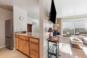 Kitchen with light stone counters, wood walls, light tile patterned floors, stainless steel refrigerator, and a fireplace