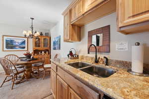 Kitchen featuring light stone countertops, sink, a notable chandelier, light colored carpet, and light brown cabinets