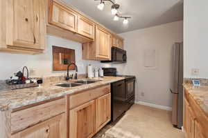 Kitchen with light tile patterned floors, black appliances, light brown cabinets, and sink