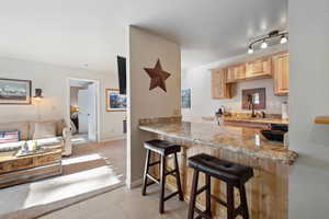 Kitchen with light stone countertops, a kitchen breakfast bar, light brown cabinetry, and kitchen peninsula