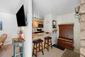 Kitchen with light stone counters, kitchen peninsula, black appliances, a breakfast bar area, and light tile patterned flooring