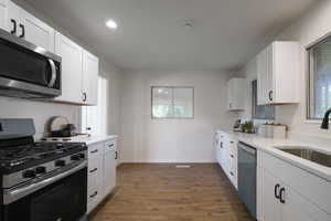 Kitchen with stainless steel appliances, white cabinets, sink, and dark wood-type flooring