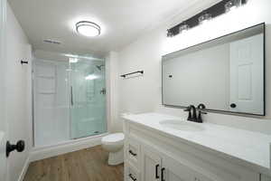 Bathroom featuring hardwood / wood-style floors, toilet, vanity, a shower with shower door, and a textured ceiling