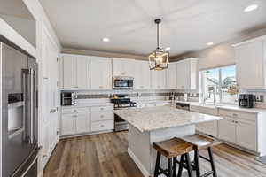 Kitchen with white cabinets, a center island, pendant lighting, and appliances with stainless steel finishes