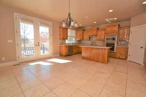 Kitchen with stainless steel appliances, a center island, pendant lighting, french doors, and an inviting chandelier