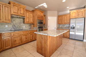 Kitchen with appliances with stainless steel finishes, a center island, light stone counters, and decorative backsplash