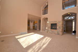 Unfurnished living room featuring a towering ceiling, a fireplace, a notable chandelier, and light carpet