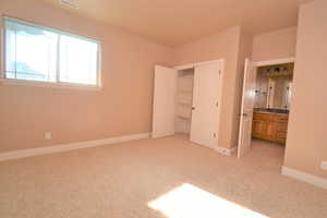 Unfurnished bedroom with light colored carpet and connected bathroom