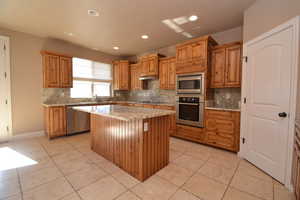 Kitchen with backsplash, a center island, light tile patterned floors, and appliances with stainless steel finishes