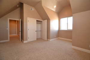 Unfurnished bedroom with lofted ceiling, a closet, and light carpet