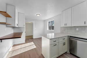 Kitchen featuring white cabinetry, kitchen peninsula, decorative backsplash, light hardwood / wood-style flooring, and stainless steel dishwasher