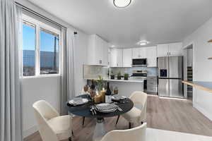 Kitchen with appliances with stainless steel finishes, white cabinetry, decorative backsplash, light hardwood / wood-style floors, and a water view