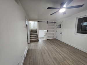 Interior space with a barn door, ceiling fan, and light hardwood / wood-style flooring