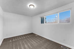 Unfurnished room with a textured ceiling and dark carpet