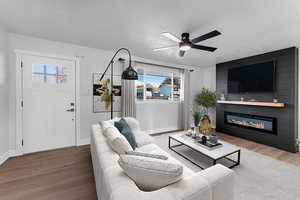 Living room featuring ceiling fan, a fireplace, a textured ceiling, and hardwood / wood-style flooring