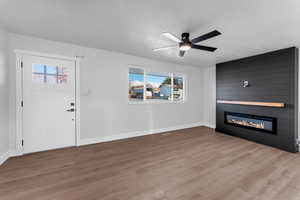 Unfurnished living room with hardwood / wood-style flooring, a textured ceiling, a large fireplace, and ceiling fan