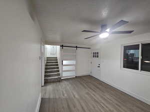 Interior space featuring ceiling fan, light hardwood / wood-style flooring, a barn door, and a textured ceiling