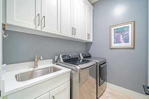 Laundry room with washer and clothes dryer, cabinets, and sink