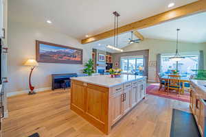 Kitchen featuring ceiling fan, light brown cabinets, vaulted ceiling with beams, a kitchen island, and hanging light fixtures