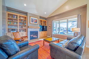 Living room with built in shelves, wood-type flooring, and lofted ceiling