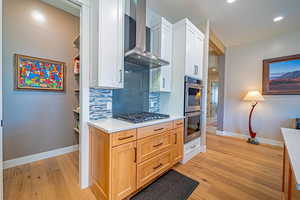 Kitchen featuring appliances with stainless steel finishes, backsplash, wall chimney exhaust hood, white cabinets, and light hardwood / wood-style floors