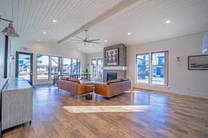 Living room featuring hardwood / wood-style floors, a tile fireplace, vaulted ceiling with beams, ceiling fan, and wood ceiling