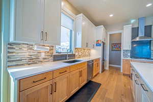 Kitchen featuring sink, wall chimney range hood, backsplash, white cabinets, and appliances with stainless steel finishes