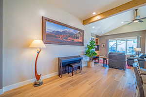 Living room with vaulted ceiling with beams, light hardwood / wood-style floors, and ceiling fan