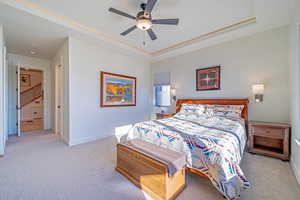 Carpeted bedroom featuring a tray ceiling, ceiling fan, and ornamental molding