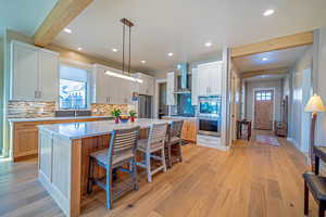 Kitchen with beam ceiling, wall chimney exhaust hood, hanging light fixtures, a kitchen island, and white cabinets