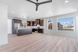 Kitchen featuring light wood-type flooring, appliances with stainless steel finishes, dark brown cabinetry, and hanging light fixtures