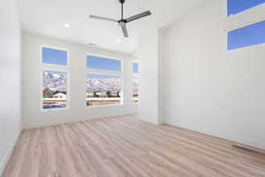 Unfurnished living room with a high ceiling, ceiling fan, and light hardwood / wood-style flooring