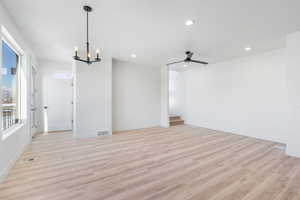 Spare room featuring ceiling fan with notable chandelier and light hardwood / wood-style floors