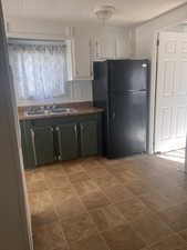 Kitchen with black fridge, white cabinetry, and sink