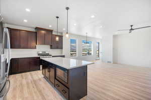 Kitchen featuring stainless steel appliances, decorative light fixtures, ceiling fan, light hardwood / wood-style floors, and a kitchen island